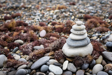 pyramid of stones on the beach against the background of a stone beach and seaweed