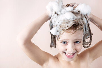 adorable little girl with blue eyes washing her hair in the bathroom and laughs, foam on the head, look at the camera