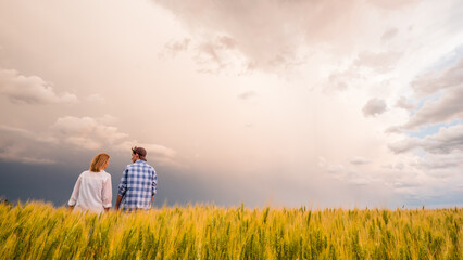 A pair of farmers stand in a field of wheat amid a dramatic stormy sky