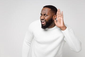 Curious shocked young african american man 20s wearing casual basic sweater standing try to hear you overhear listening intently looking camera isolated on white color wall background studio portrait.