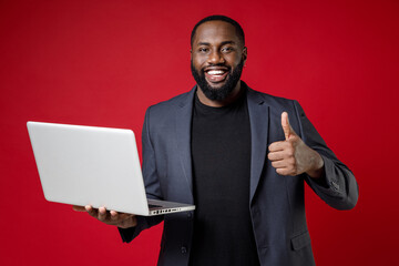 Smiling young african american business man 20s in classic jacket suit standing working on laptop...