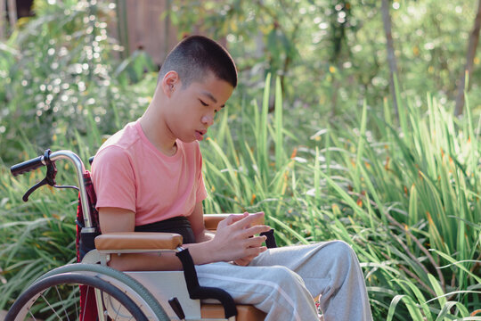 Asian Special Child On Wheelchair Wearing Sweet Pink T Shirt In Moody Sad Swings Like Other Teenagers With Green Fields Background, Lifestyle In The Education Age Of Disabled Children.