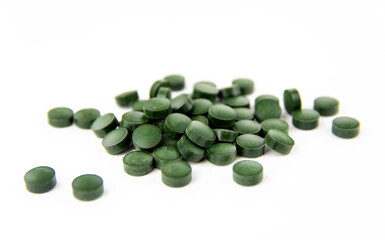 Green spirulina pills are scattered on a white background. Copy space.