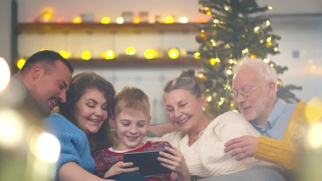 Happy family gathered on couch together using tablet watching christmas photos