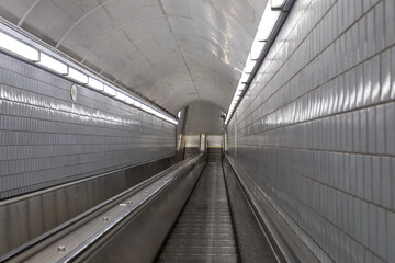 Grey tiled wall and overhead lights of long escalator leading to underground subway station