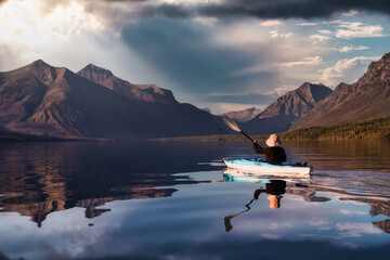 Adventurous Man Kayaking in Lake McDonald with American Rocky Mountains in the background. Colorful Sunset Sky. Taken in Glacier National Park, Montana, USA.