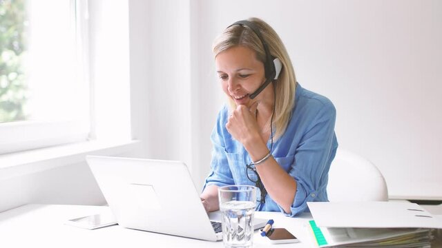 Businesswoman sitting at desk using headset and laptop