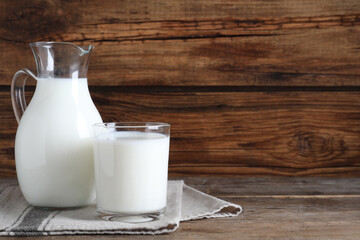 Jug and glass with fresh milk on wooden table. Space for text