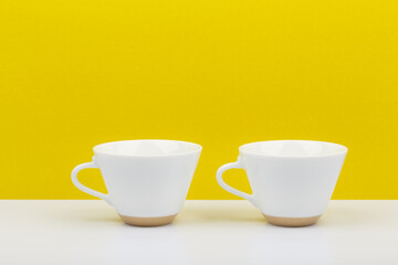 Two white cups of coffee in a row against yellow background. Still life with a space for text