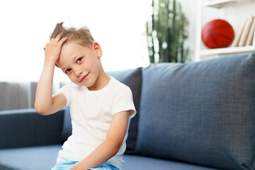 Cute little boy sitting on couch at home, looking at camera