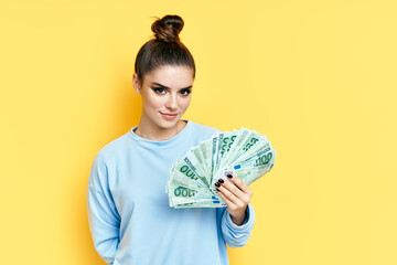 Young pretty woman holding money banknotes on yellow background