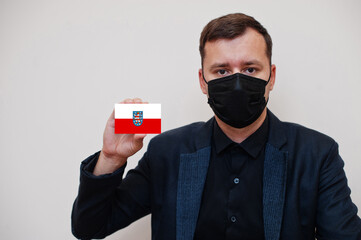 German man wear black formal and protect face mask, hold Thuringia flag card isolated on white...