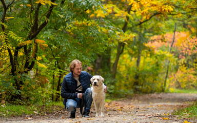 Handsome young man with dog outdoors. Man in an autumn park with dog labrador retriever.