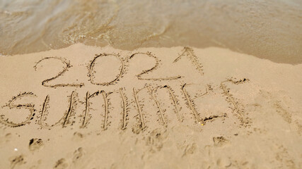 word handwritten summer 2021 on yellow sandy beach