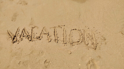 Text Vacation written in the sand of sea beach