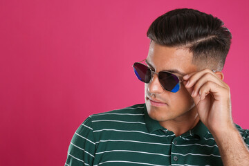 Handsome man wearing sunglasses on pink background, closeup. Space for text