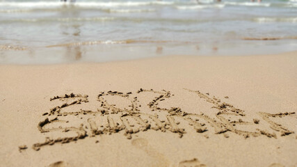 word handwritten summer 2021 on yellow sandy beach