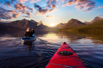 Adventurous Man Kayaking in Lake McDonald with American Rocky Mountains in the background. Colorful...