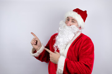 Fototapeta na wymiar Man dressed as Santa Claus standing over isolated white background pointing to the side
