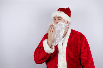 Man dressed as Santa Claus standing over isolated white background bored yawning tired covering mouth with hand. Restless and sleepiness.