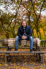 Fototapeta premium Young man sitting on a park bench. Golden autumn and sunny days. Portrait of a handsome male.