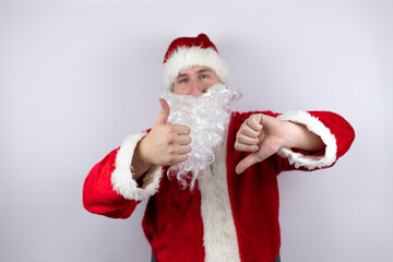 Man dressed as Santa Claus standing over isolated white background Doing thumbs up and down, disagreement and agreement expression. Crazy conflict