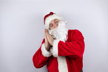 Man dressed as Santa Claus standing over isolated white background sleeping tired dreaming and posing with hands together while smiling with closed eyes.