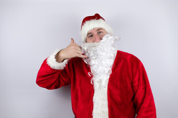 Fototapeta na wymiar Man dressed as Santa Claus standing over isolated white background smiling doing phone gesture with hand and fingers like talking on the telephone