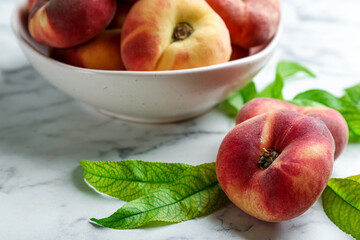 Fresh ripe donut peaches with leaves on white marble table, closeup