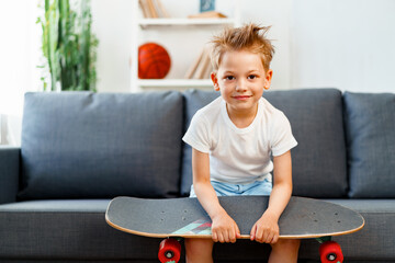 Little boy sitting on sofa at home and holding skateboard