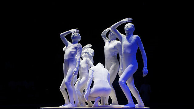 A group of people in skin-tight, covering their faces, white catsuits on a black background. Fear of a meteorite or unknown future