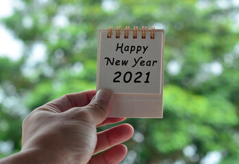 Hands Holding Calendar 2021 with blurred green background. Happy New Year 2021