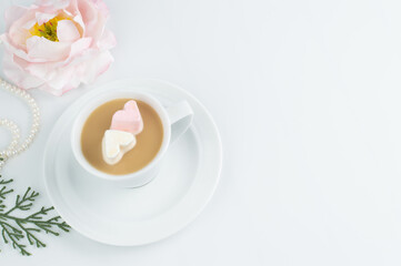 On a white background, a blurred image of a cup with cocoa and marshmallows in the shape of hearts, peony, pearls and green beads.