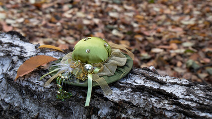 Cute small  vintage green satin hat with ribbons feather and decoration lies on a birch log in the autumn forest. 