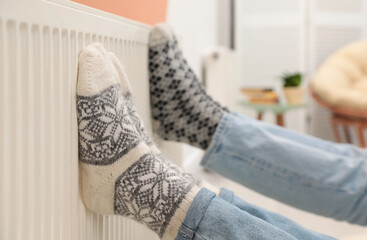 Couple warming legs on heating radiator indoors, closeup