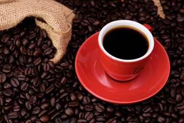 Red coffee cup with black needle coffee with saucer and fragrant roasted coffee beans on the needle colored table - top view with copy space.