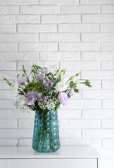 Bouquet of beautiful Eustoma flowers on cabinet near white brick wall
