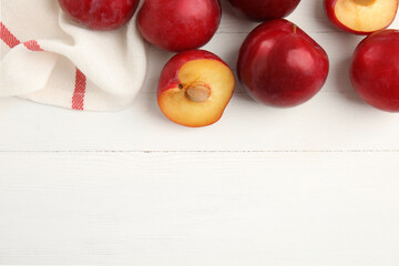 Delicious ripe plums on white wooden table, flat lay. Space for text