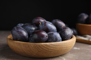 Delicious ripe plums in wooden bowl on grey marble table, closeup