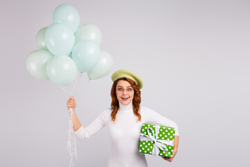 Portrait of pretty cheerful wavy-haired girl holding in hands giftbox air helium balls isolated over light white gray color background
