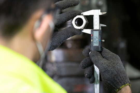 closeup behind engineer man or factory worker using calipers measures the external dimension of the nut