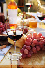 Red wine and snacks served for picnic on wooden table outdoors