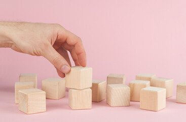 Obraz premium Wooden cubes on a pink background. The hand puts the cube. Place for text