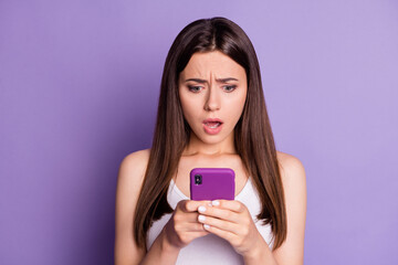 Fototapeta premium Photo of unhappy astonished brown haired woman look phone bad message post isolated on purple color background