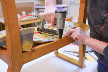 Renovation of old upholstery. Woman hands working in upholstery workshop. Making new upholstery on old chair. Yellow fabric. Work with pneumatic stapler. 