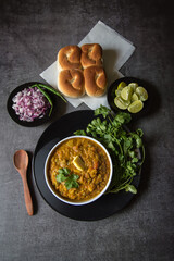 View from top of spicy pav bhaji or masala dish and bread in a bowl on a black plate with use of selective focus. 