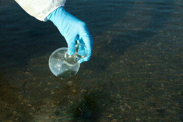 Scientist with florence flask taking sample from river for analysis, closeup