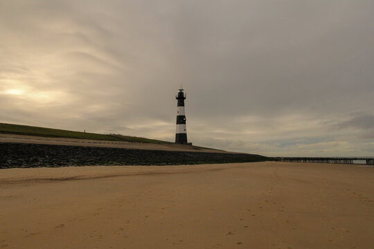 a coast landscape with a large sand beach and a lighthouse at the seawall and a grey sky in winter in breskens