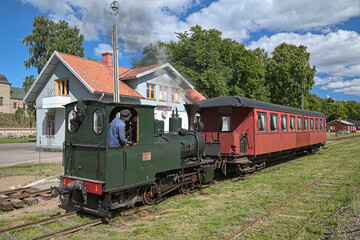 Fototapeta na wymiar Old steam locomotive with passenger coach at Vadstena station of the narrow-gauge railway Vadstena-Fagelsta, Sweden. The railway was put into operation in 1874.