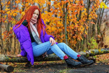 Teen girl in violet jacket sitting on log - 396347690